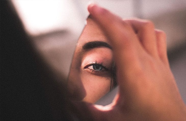 A woman holding a broken piece of mirror showing her eyes