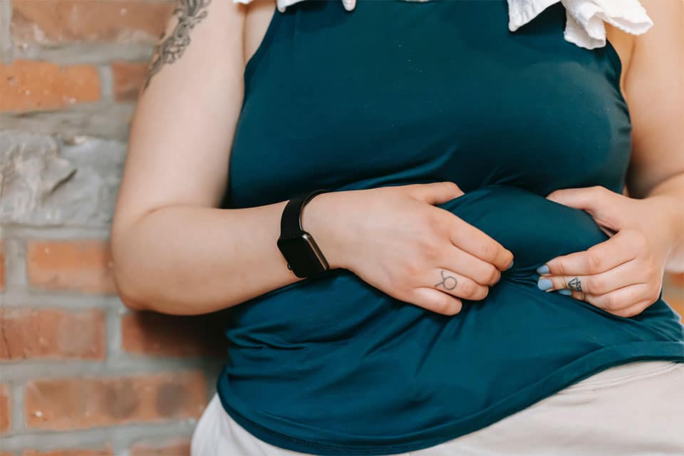 photo of a woman showing overweight belly near brick wall