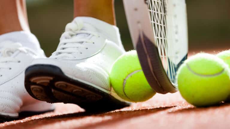 Legs of athletic girl near the tennis racket and balls