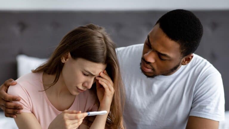 Upset man comforting his depressed wife with negative pregnancy test in bedroom