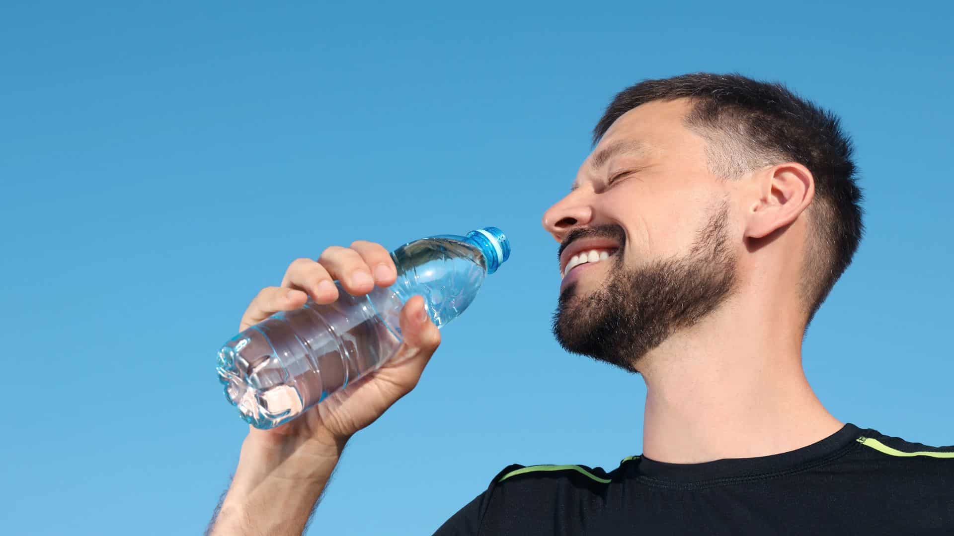 man drinking water against blue sky on hot summer day