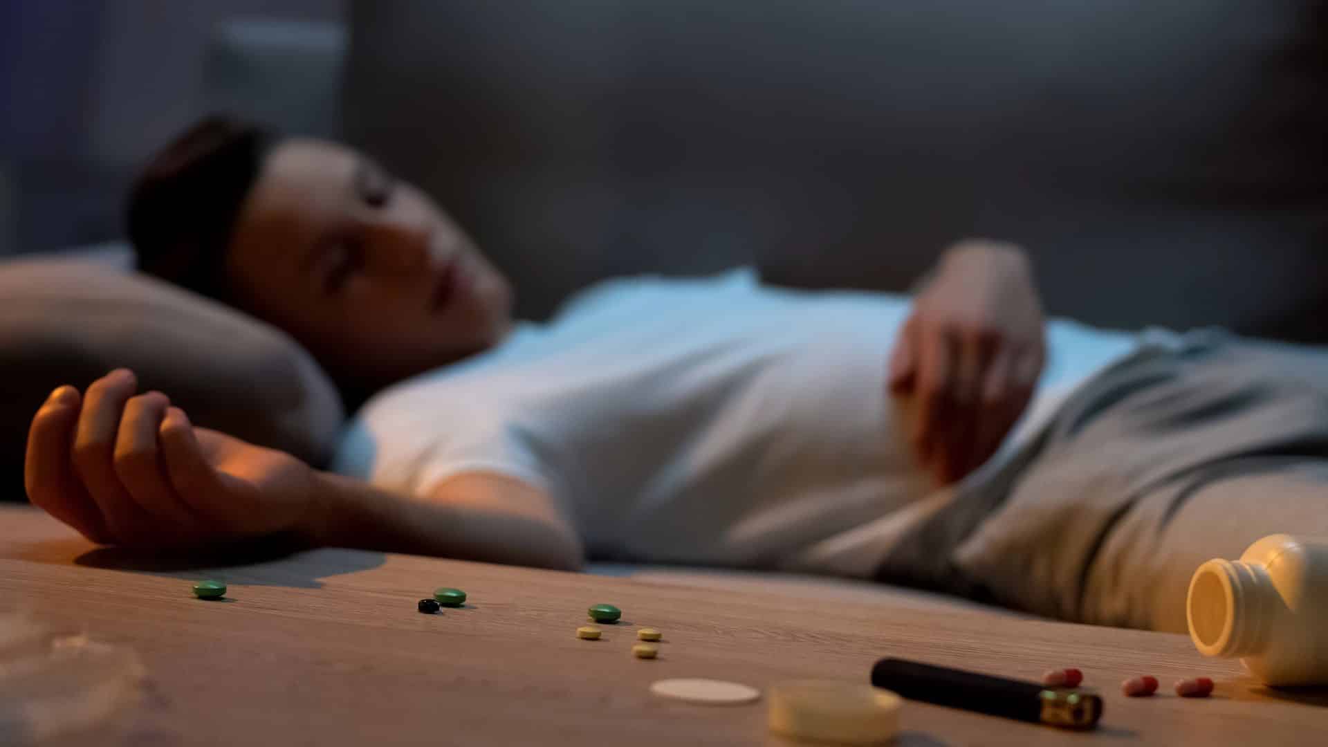 Teen boy sleeping at home, pills spilled on table