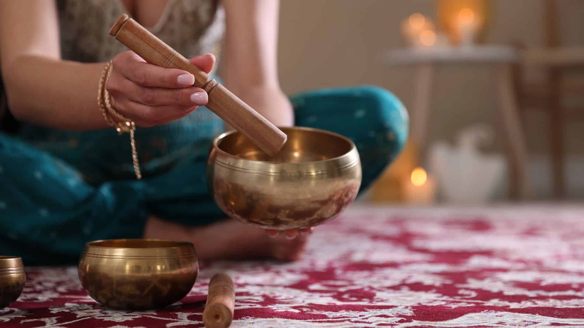 Woman with singing bowls and burning candles indoors