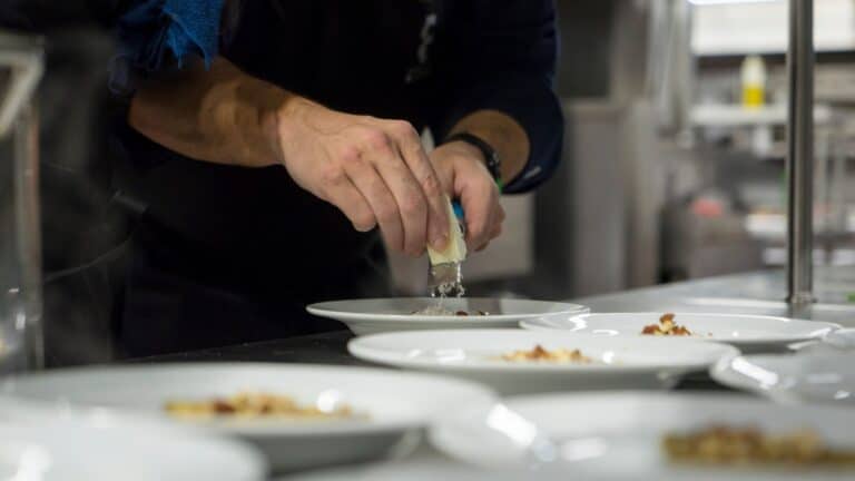 Chef grating parmesan over plates illustrating chef-prepared meals for addiction recovery.