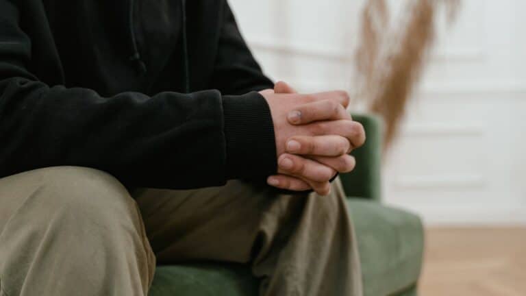 person sitting indoors with hands clasped