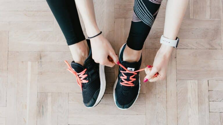 A woman ties her sneakers on a wooden floor