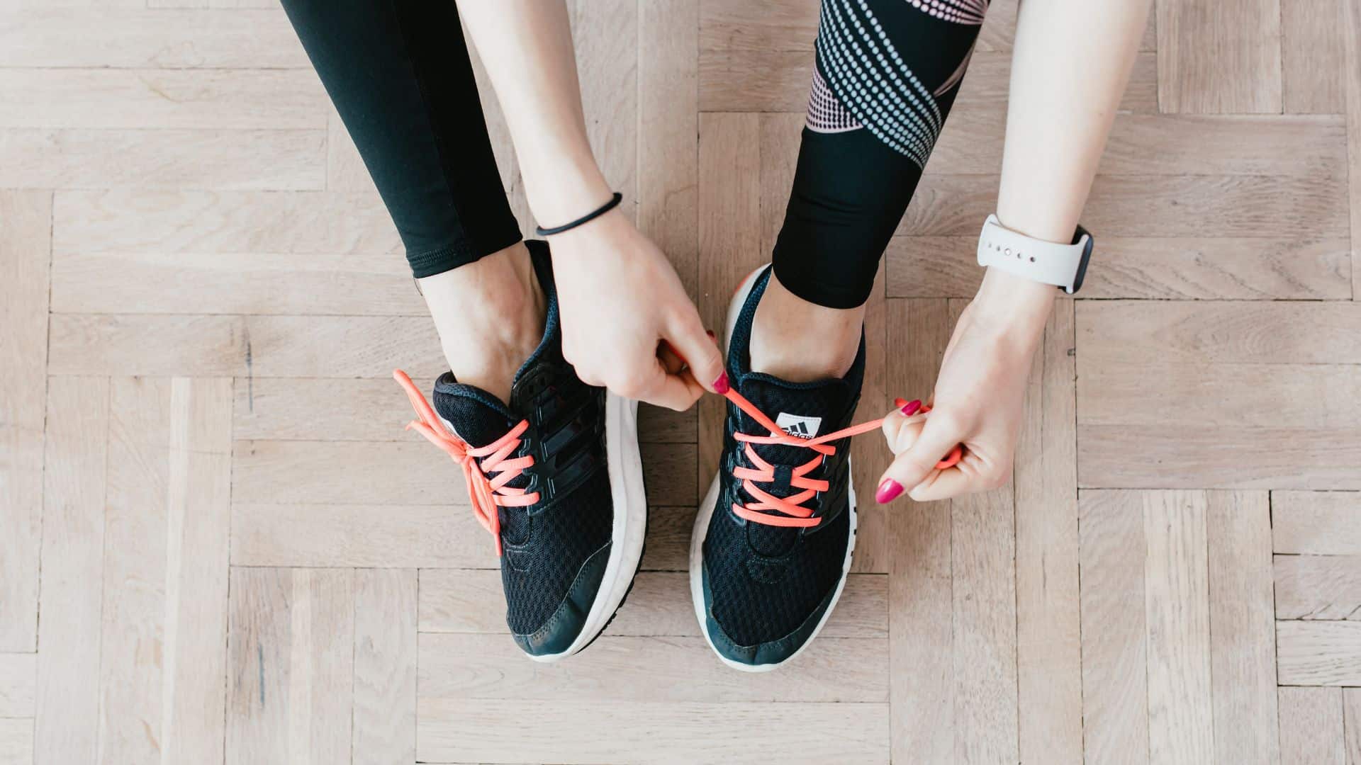 A woman ties her sneakers on a wooden floor